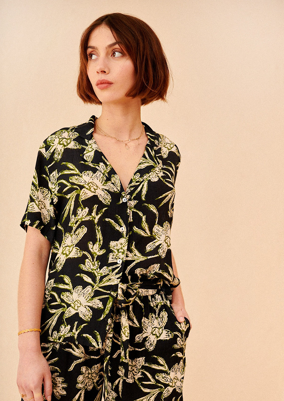 A woman wearing a v-neck collared shirt in black with green and cream floral print.