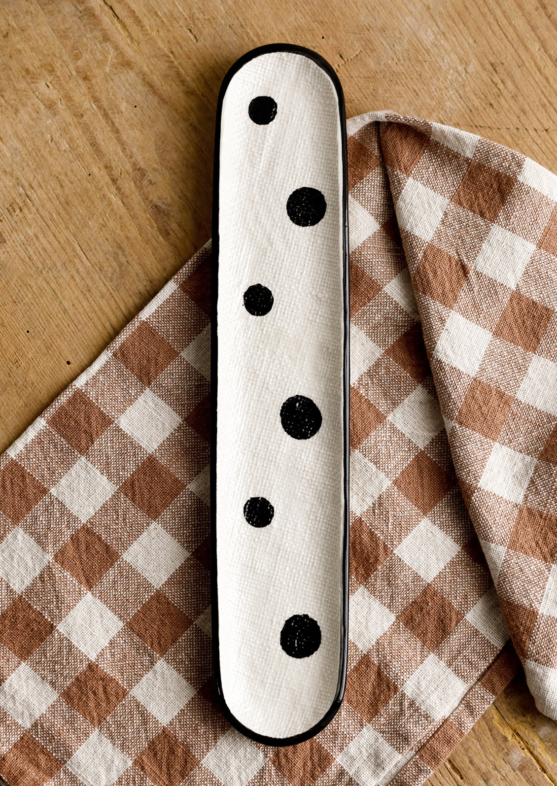 An oblong, skinny ceramic platter in cream with black polka dot print.