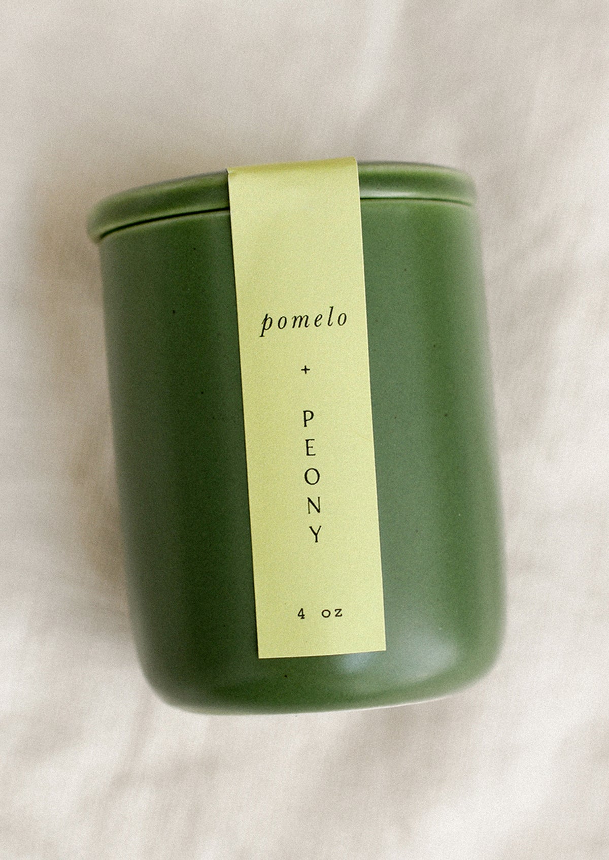 A small candle in lidded green ceramic jar in Pomelo & Peony scent.
