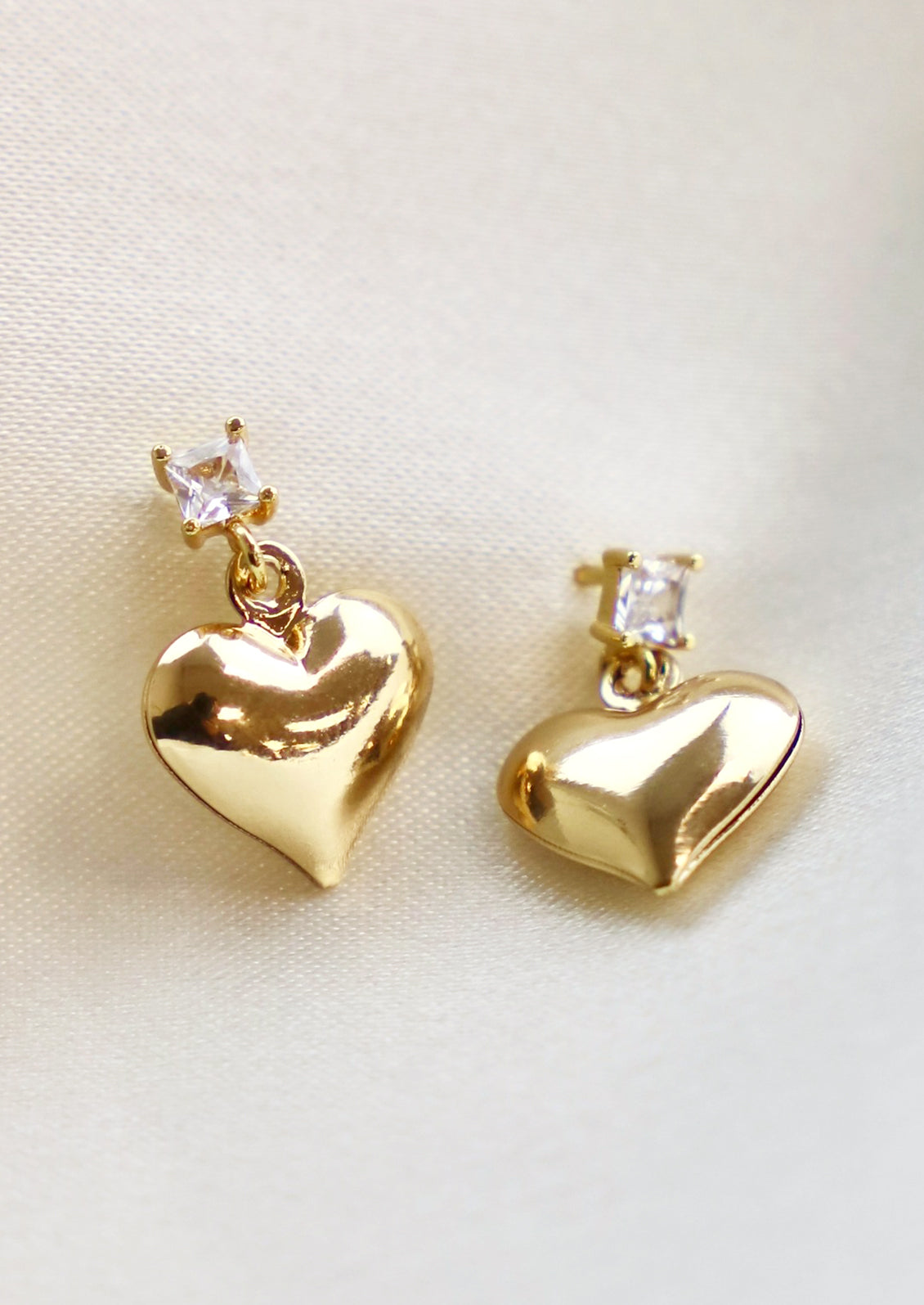 A pair of gold heart earrings hanging from square crystal post.