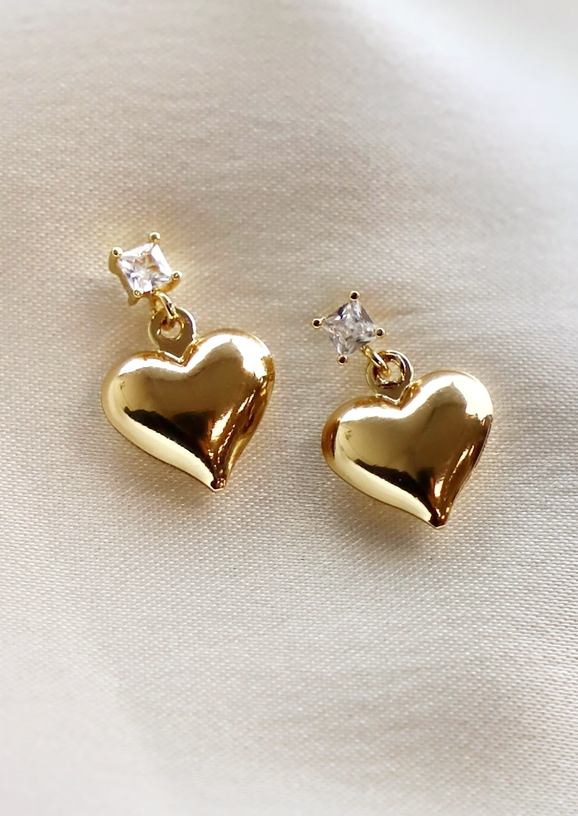 A pair of gold heart earrings hanging from square crystal post.