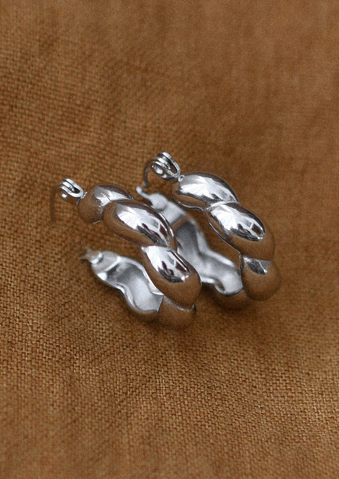 A pair of silver hoop earrings with puffy twist texture.