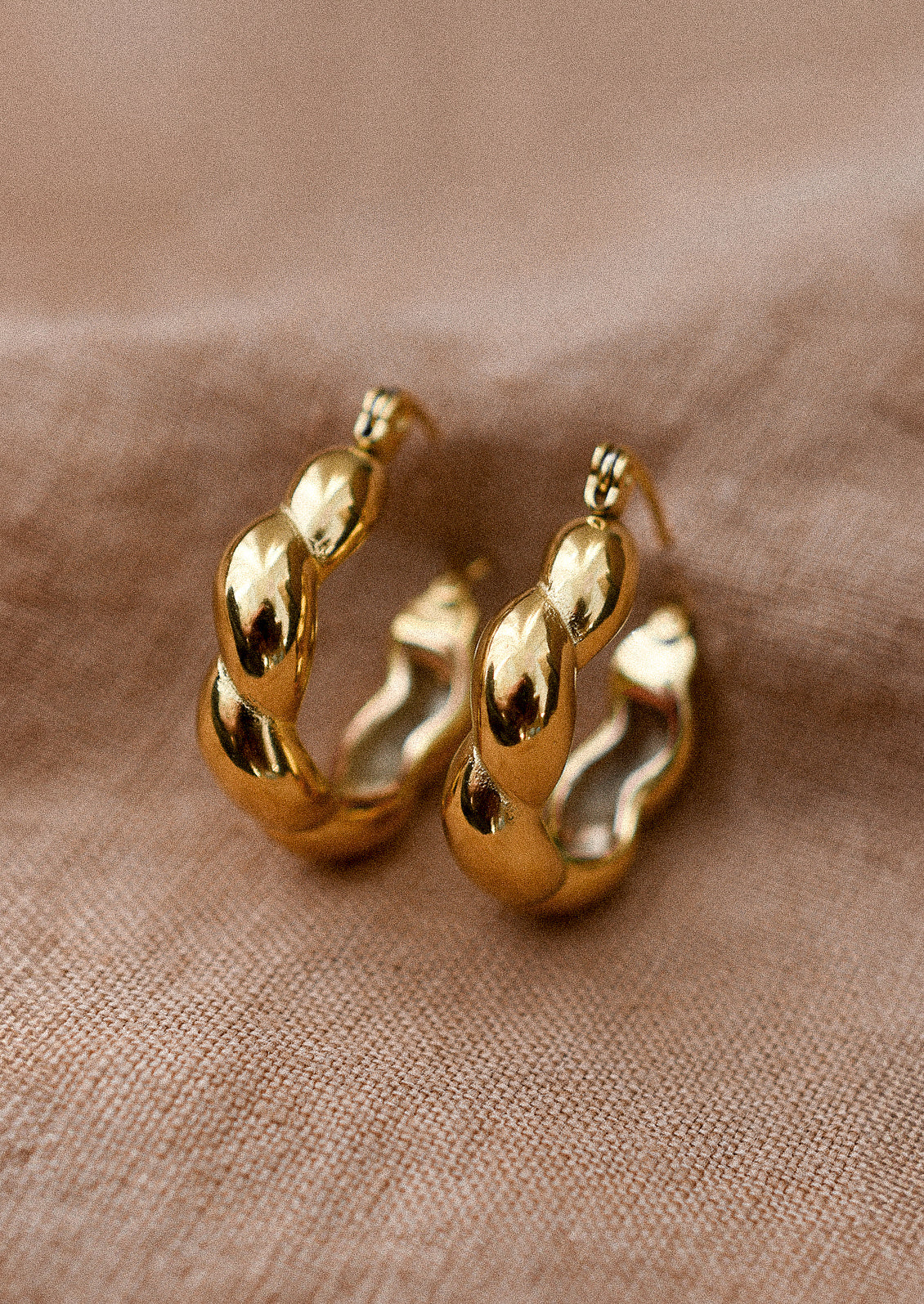 A pair of gold hoop earrings with puffy twist texture.