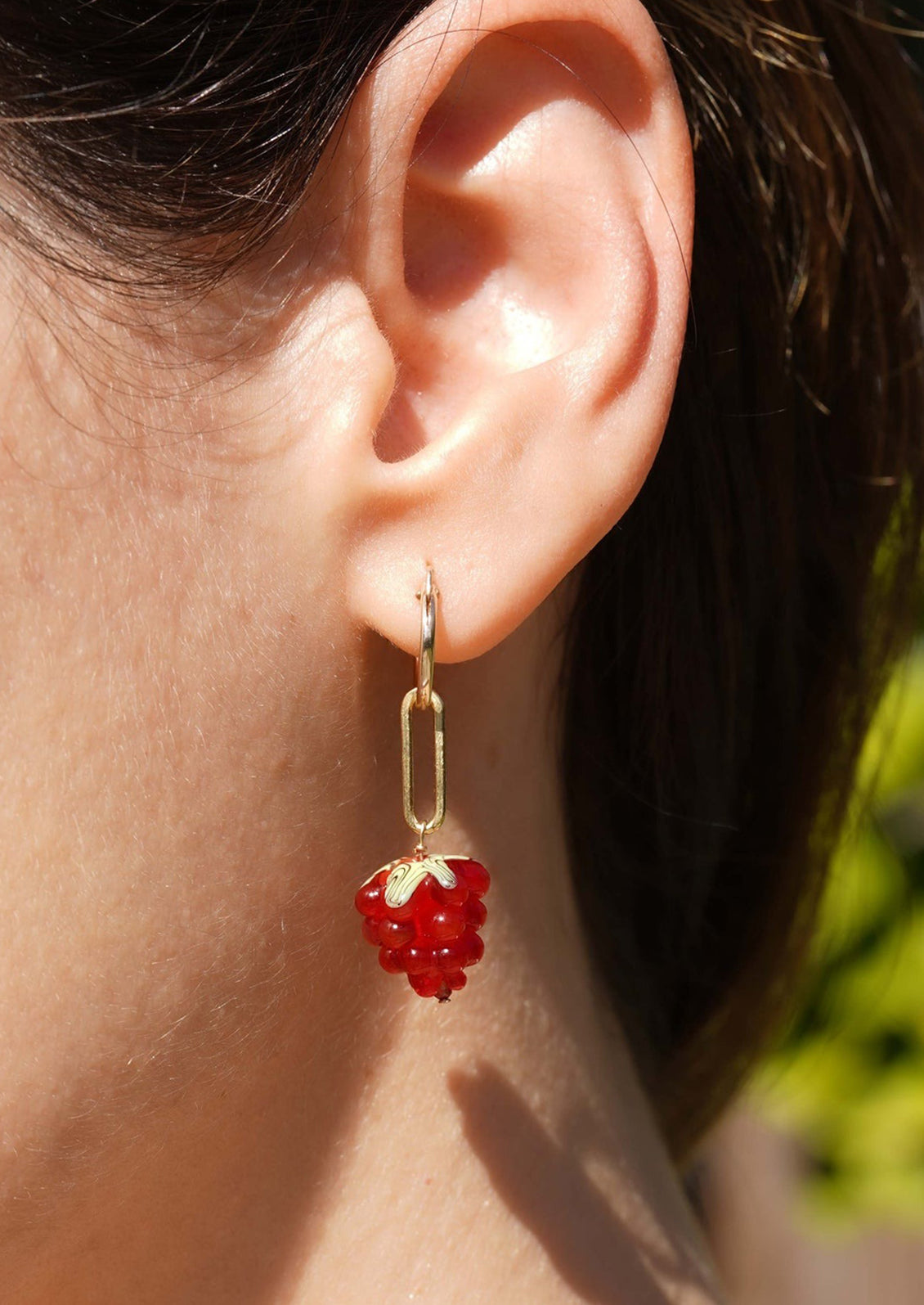 A pair of gold earrings with glass raspberry charm.