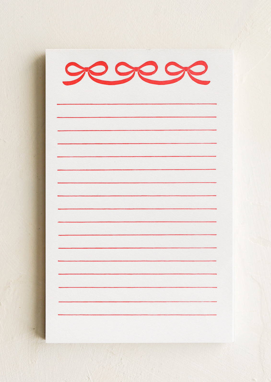 A ruled notepad with red bow print at top.