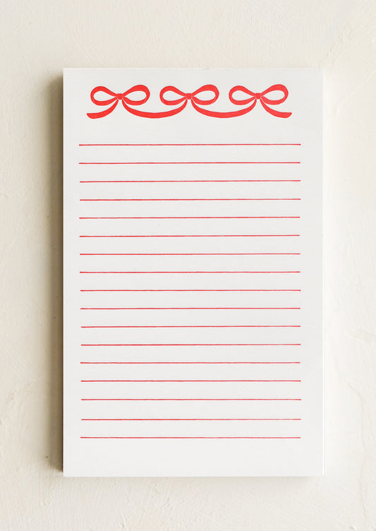 A ruled notepad with red bow print at top.