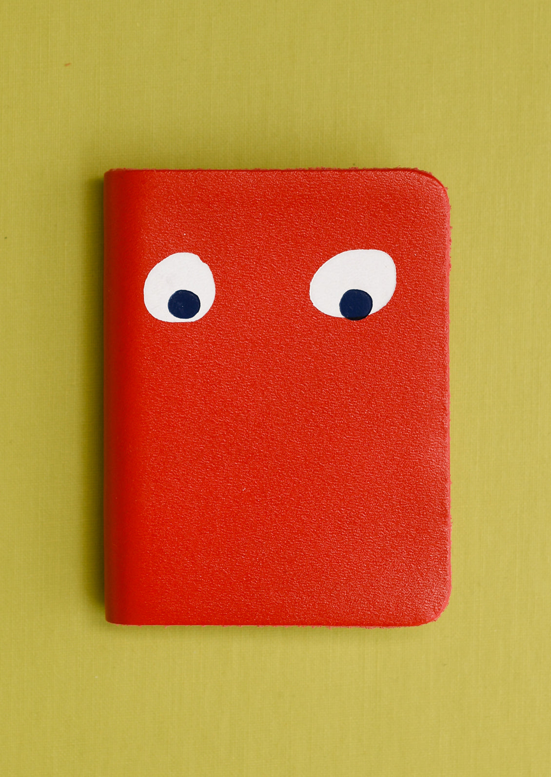 A red leather notebook with pair of eyes painted on cover.