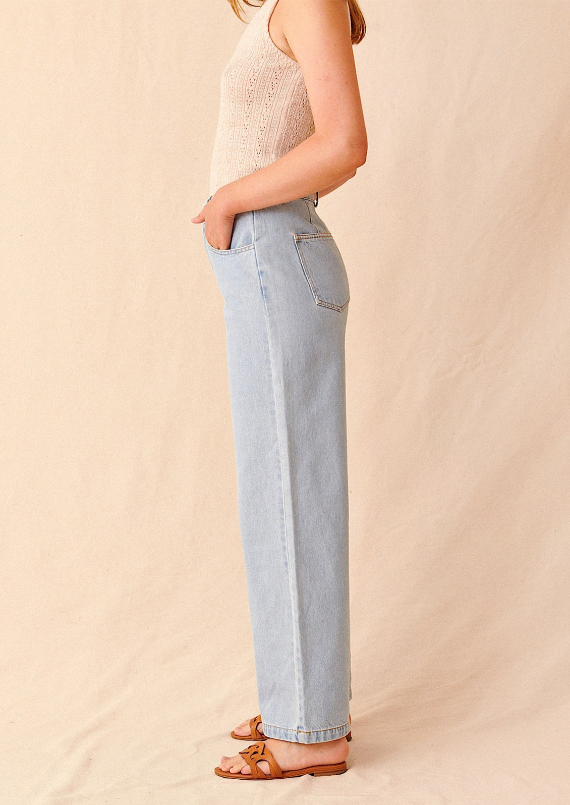 Woman wearing light wash jeans and sandals, seen from the side. 