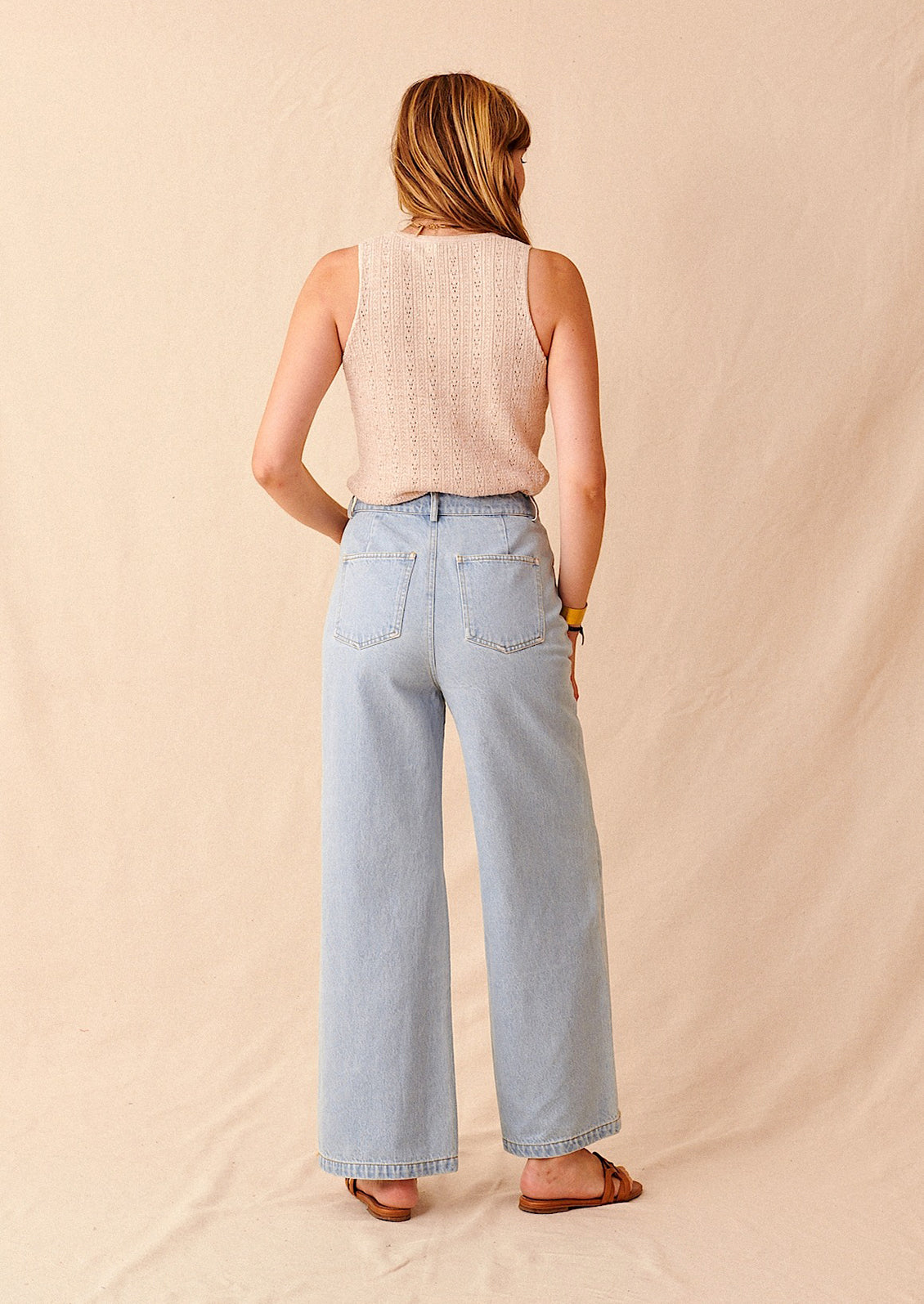Woman wearing light wash jeans, tank, and sandals, seen from behind. 