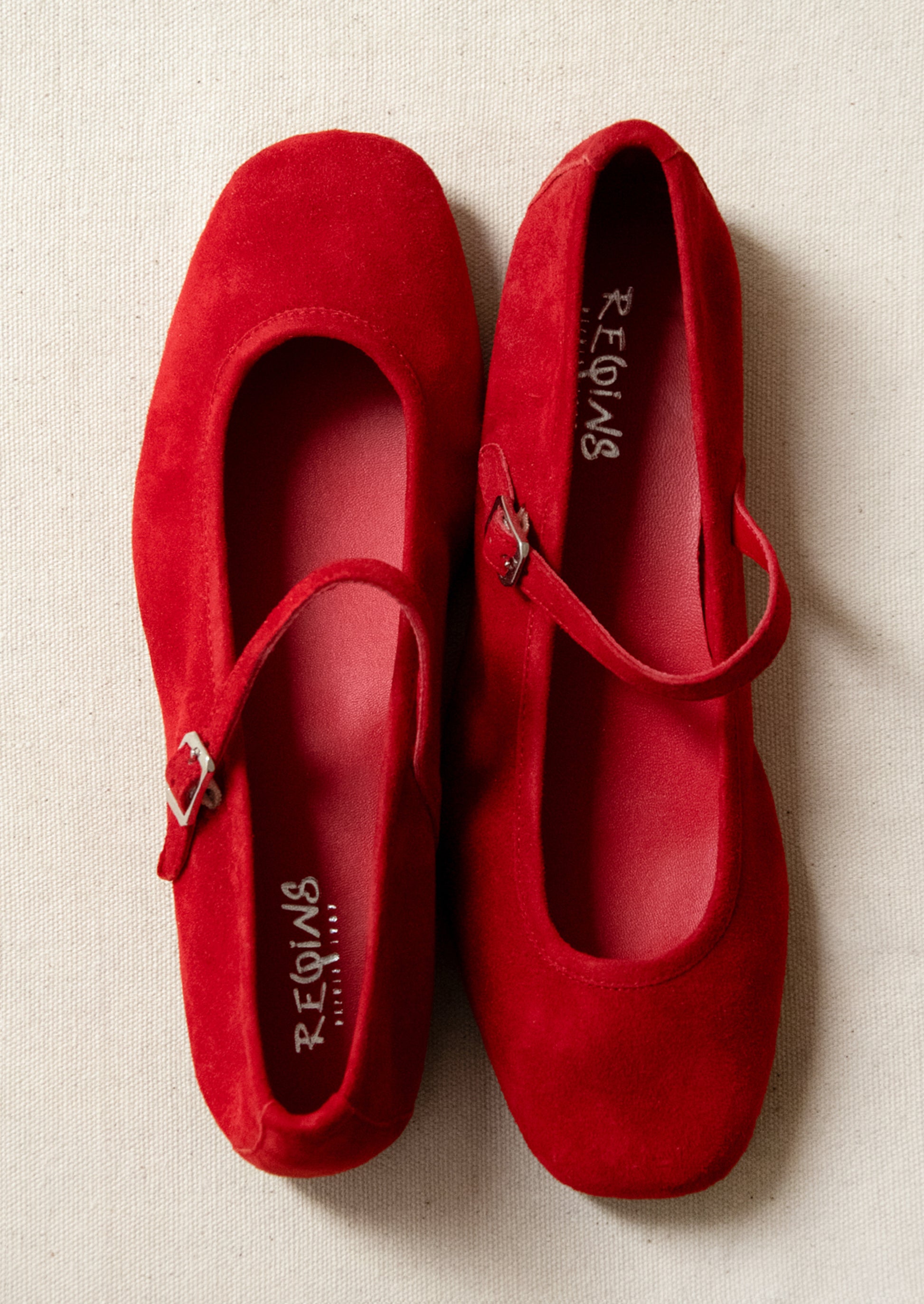 A pair of red suede mary jane flats.