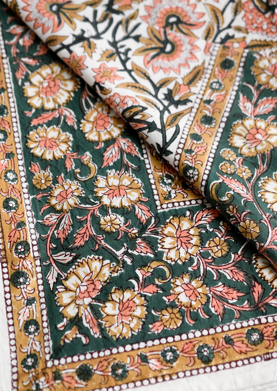 A block printed floral tablecloth in peach, brown and emerald.
