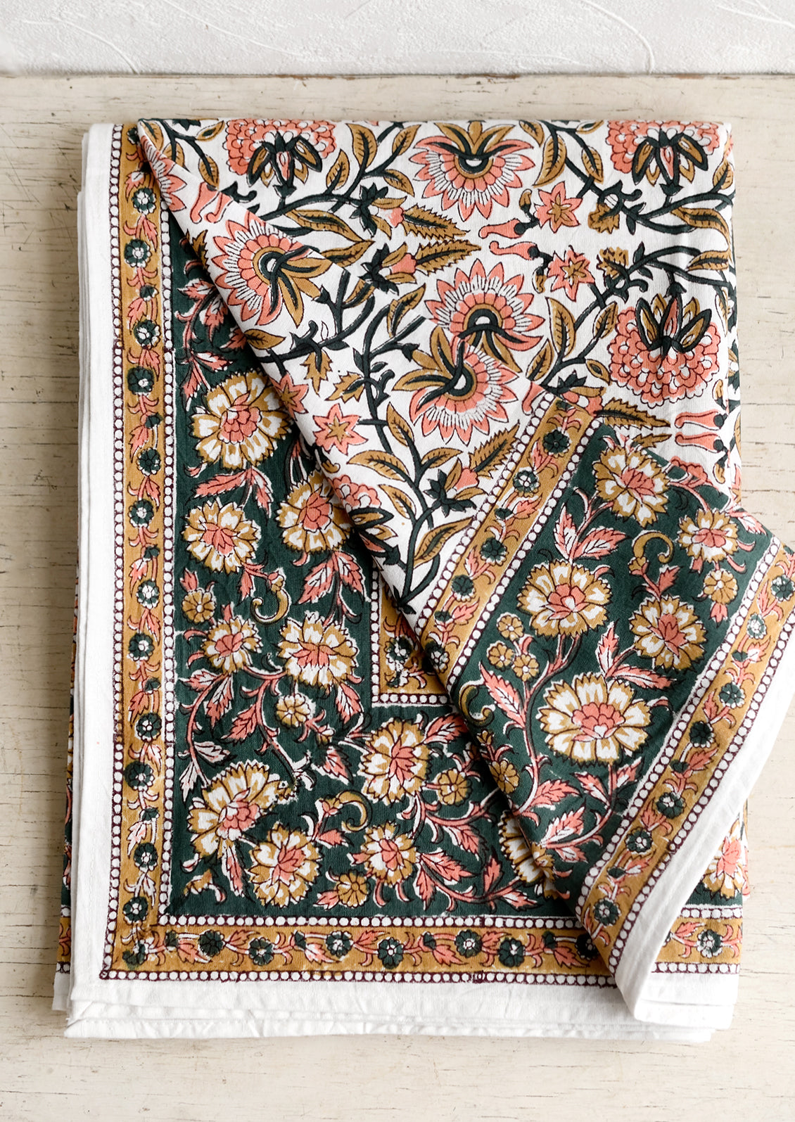 A block printed floral tablecloth in peach, brown and emerald.