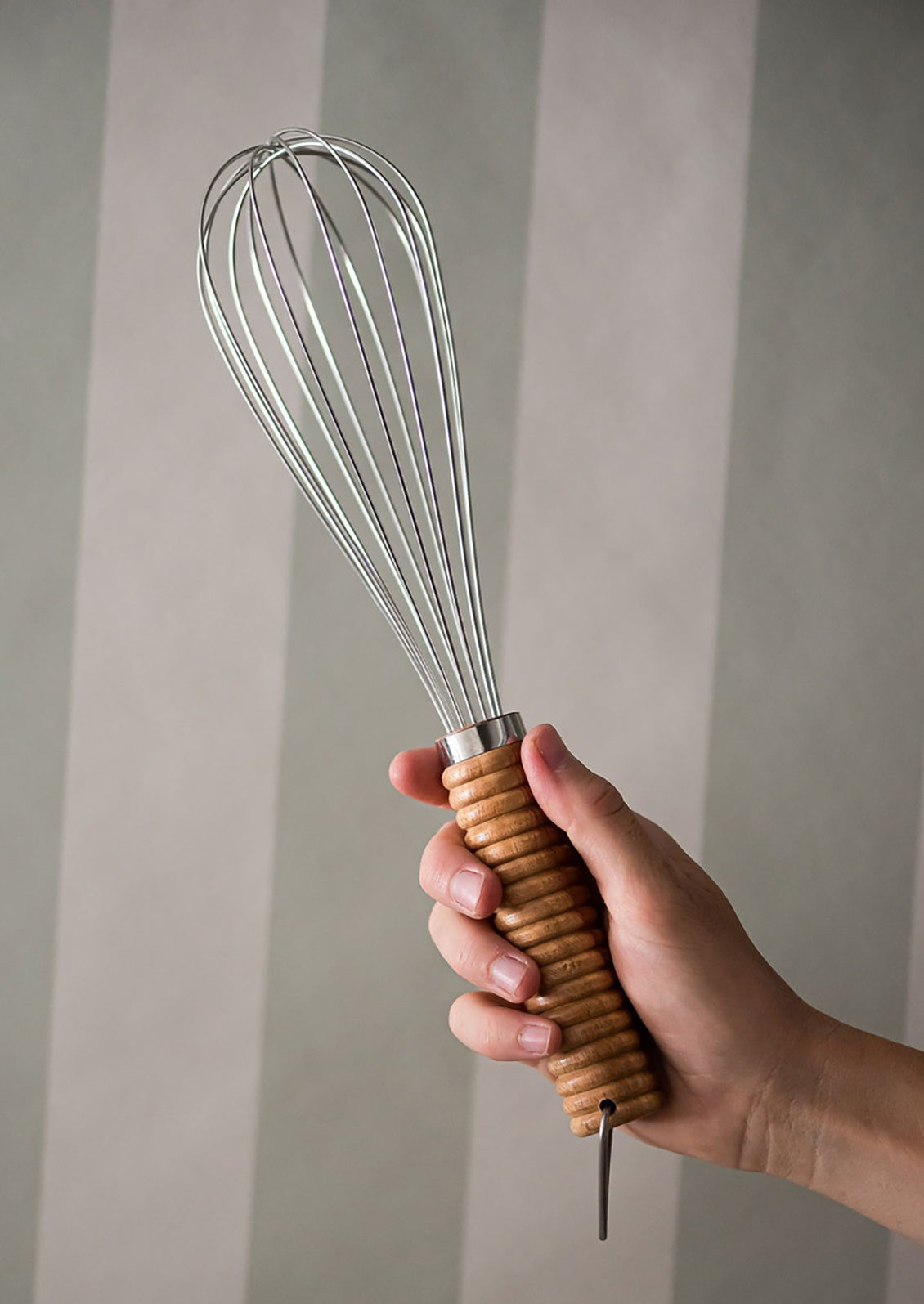 A stainless steel whisk with ribbed wooden handle.