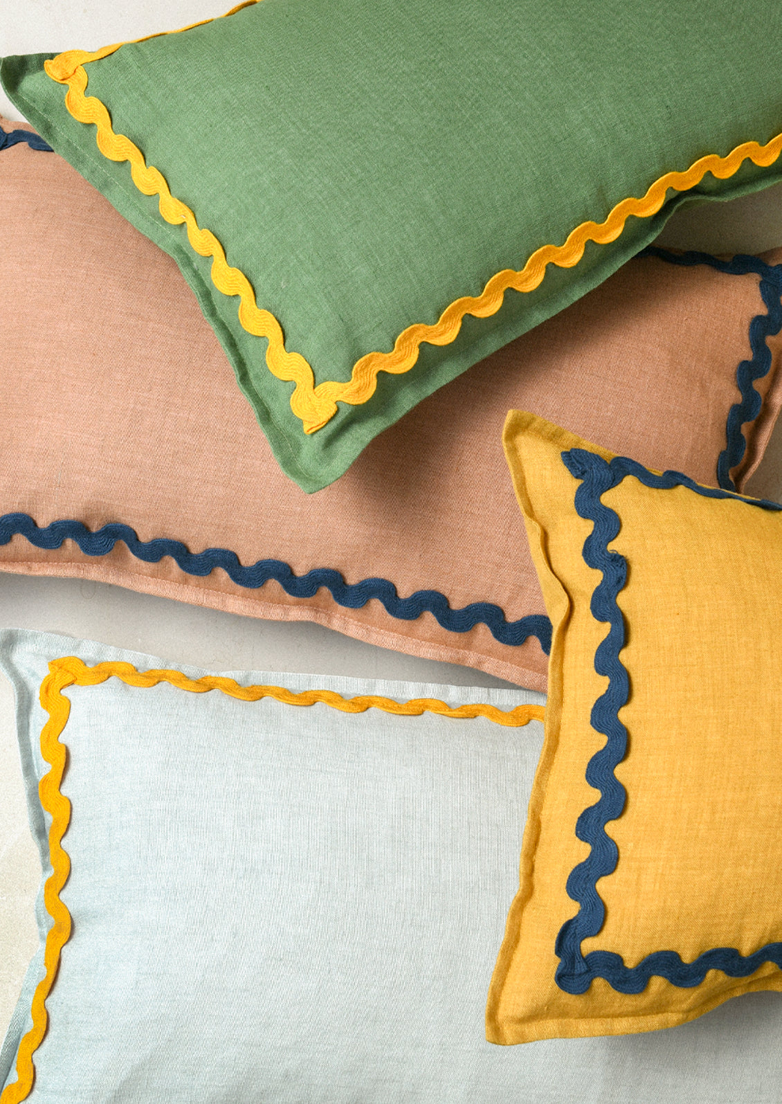 Four colorful rectangular linen pillows with a squiggle border attached along the edges.