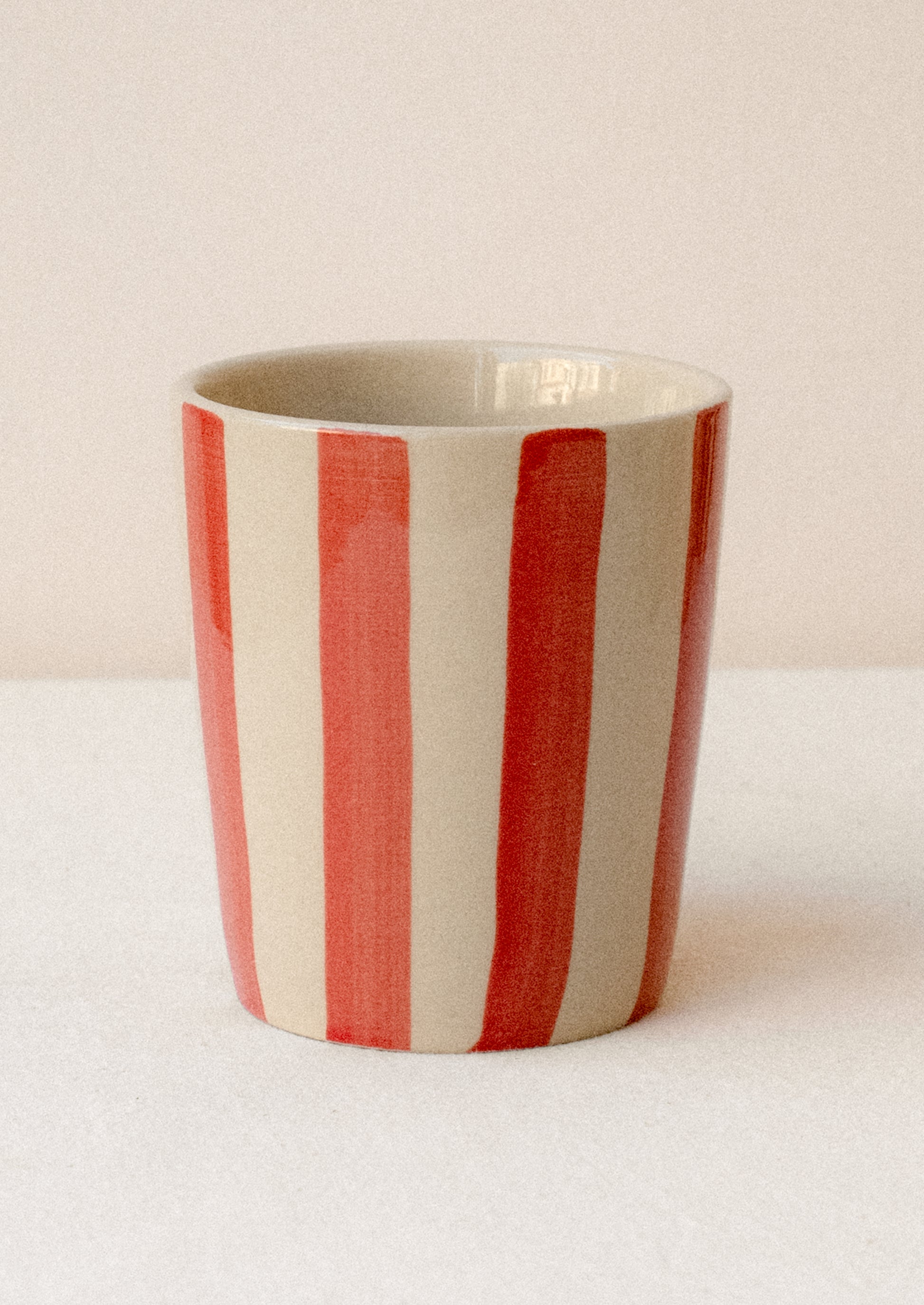 A striped ceramic cup in bisque with red vertical stripes.