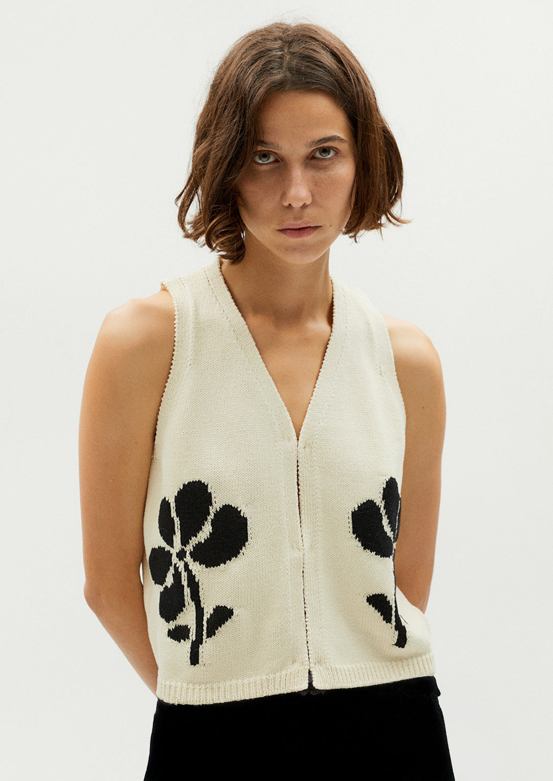 A woman wearing a sleeveless v-neck top in cream with black jacquard flower pattern.