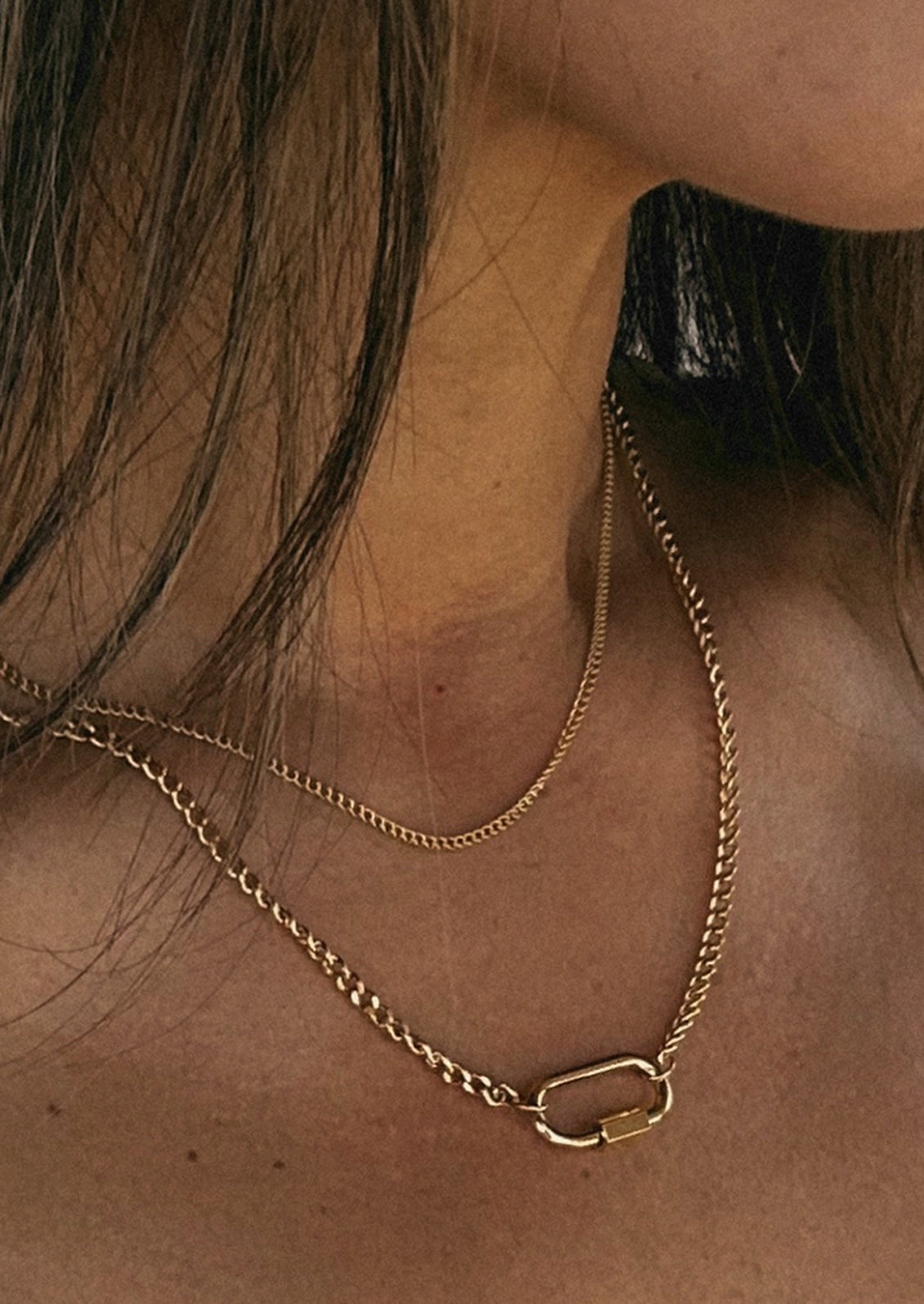 A layered gold chain necklace with a carabiner charm.