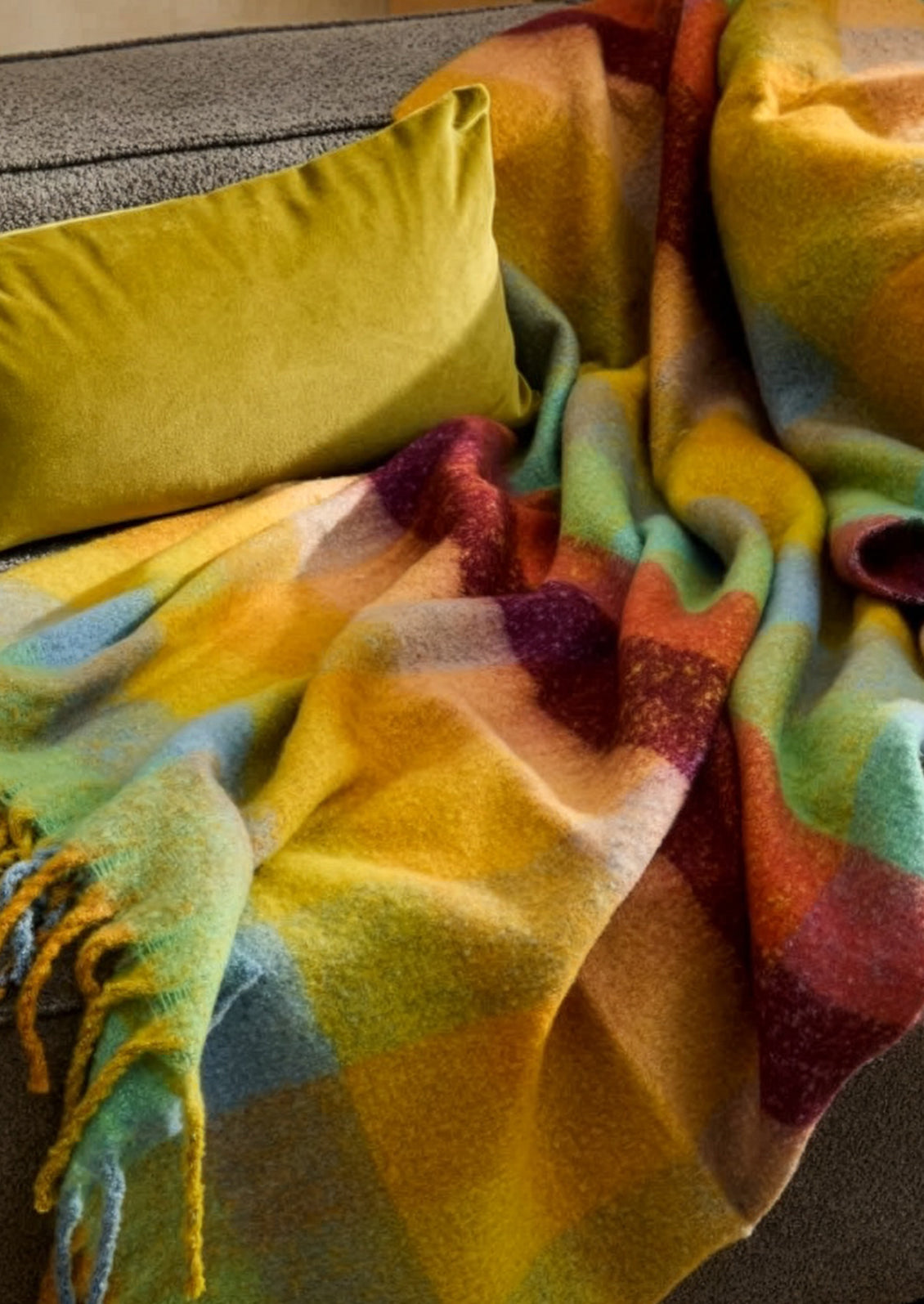 Colorful plaid blanket draped over a surface with a yellow pillow.