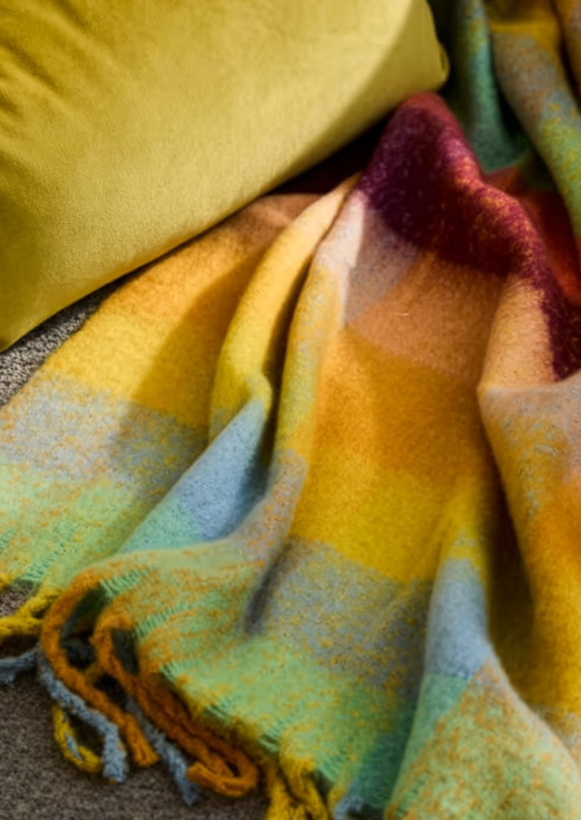 Colorful plaid blanket with a gradient of yellow, green, and red on a textured surface.
