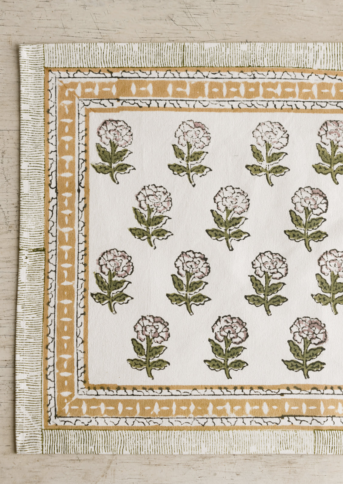 A block printed placemat in floral print in green and purple with mustard border.
