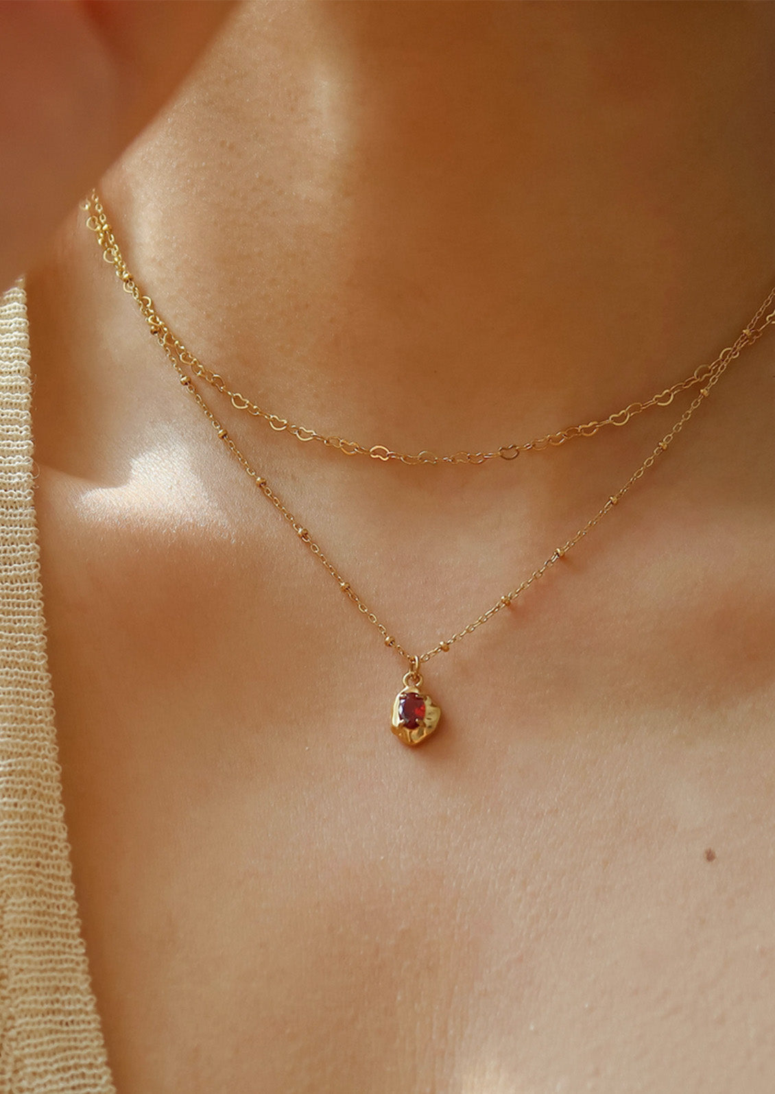 A gold necklace with a red gemstone pendant.