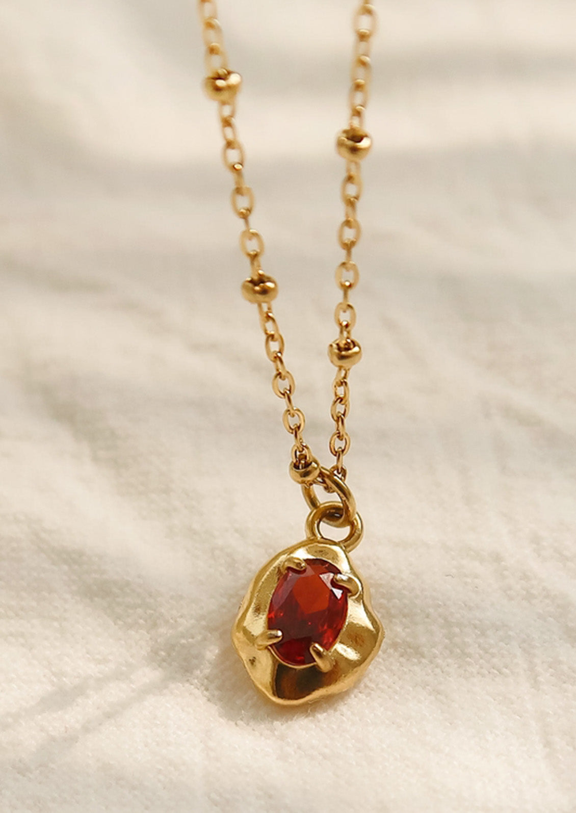 A gold necklace with a red gemstone pendant.