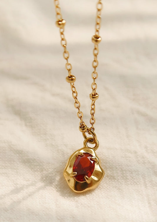 A gold necklace with a red gemstone pendant.