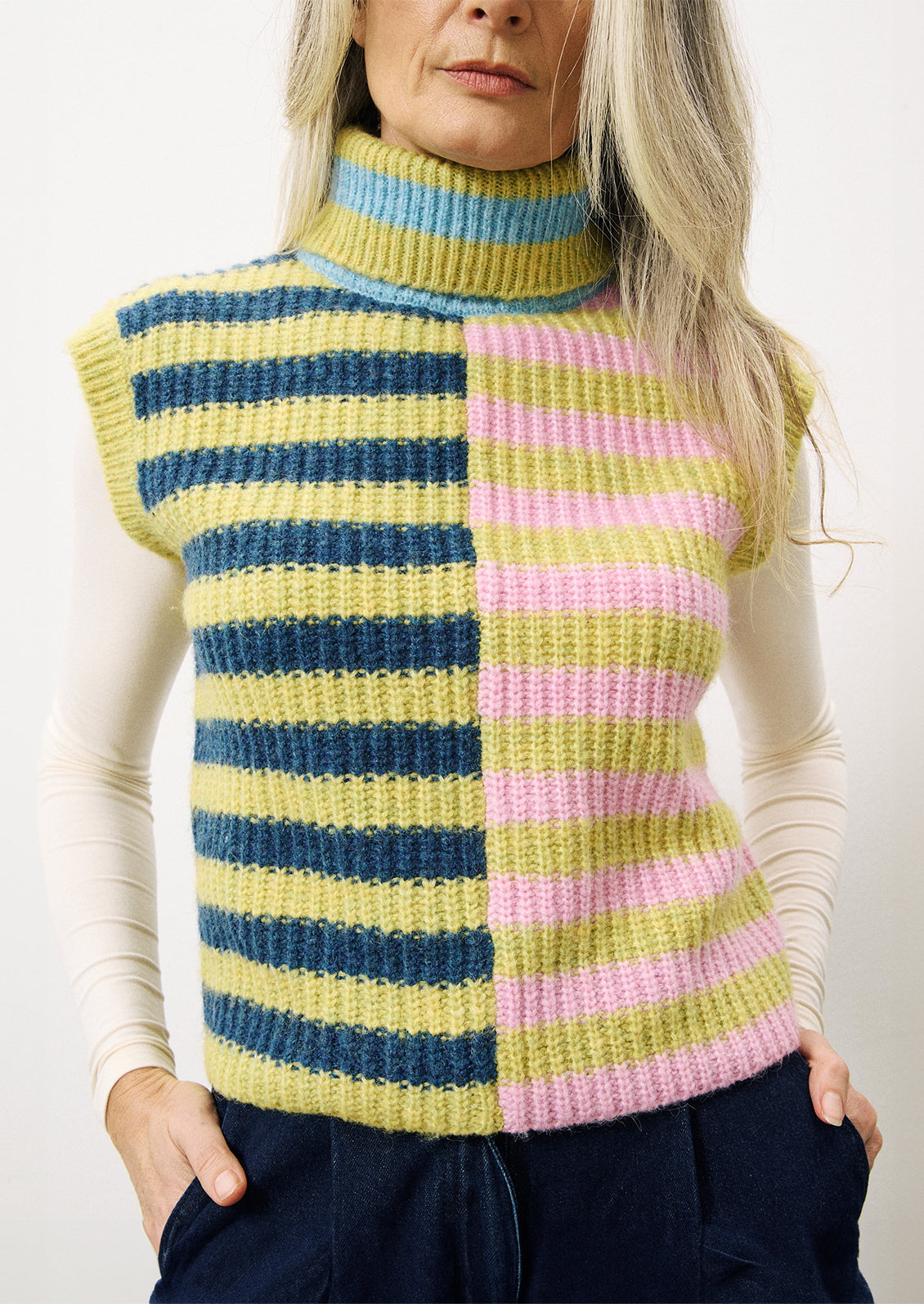 A woman wearing a lime green, navy and pink stripe sleeveless sweater vest with turtleneck.