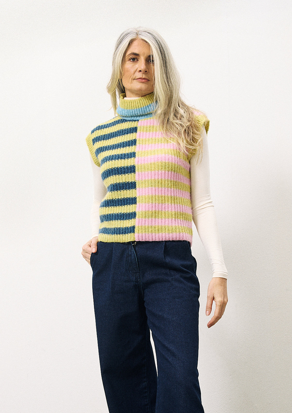 A woman wearing a lime green, navy and pink stripe sleeveless sweater vest with turtleneck.