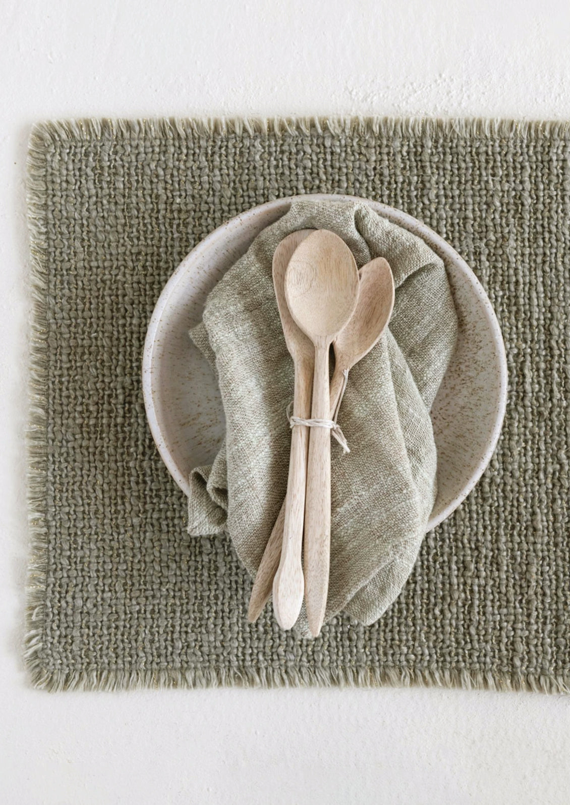 A sage green placemat with fringe edges.