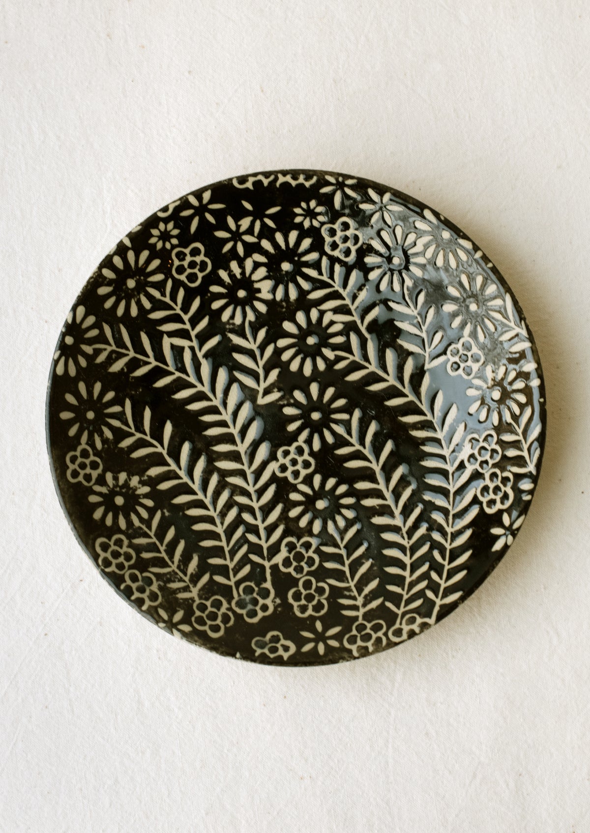 A small side plate with wax relief floral pattern in black and white.