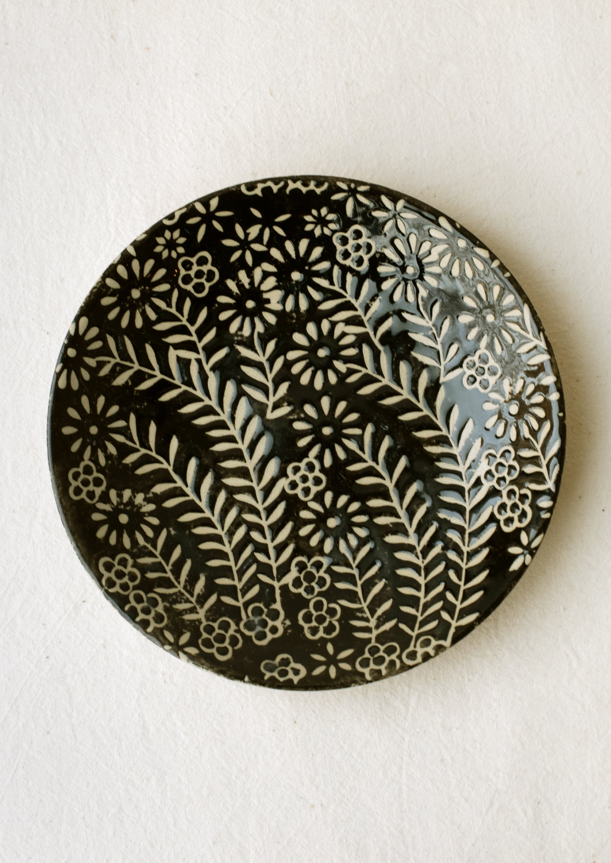A small side plate with wax relief floral pattern in black and white.