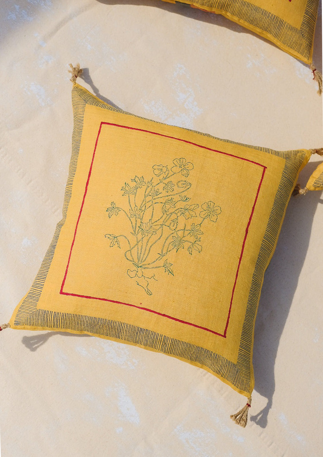 A yellow throw pillow in linen with framed floral outline.
