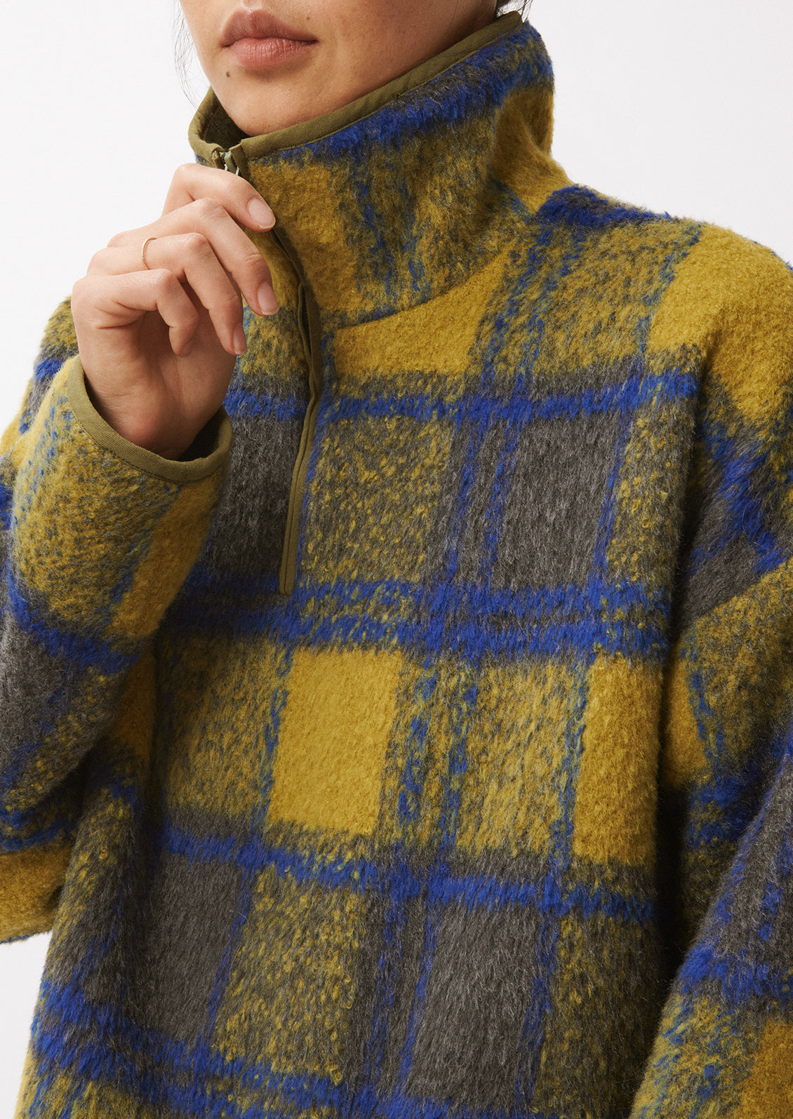 A woman wearing a fleece pullover in olive and cobalt blue plaid pattern.