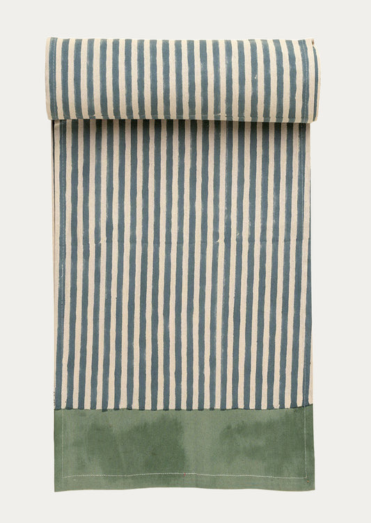 Striped fabric table runner with blue and white stripes and a green bottom section on a white background