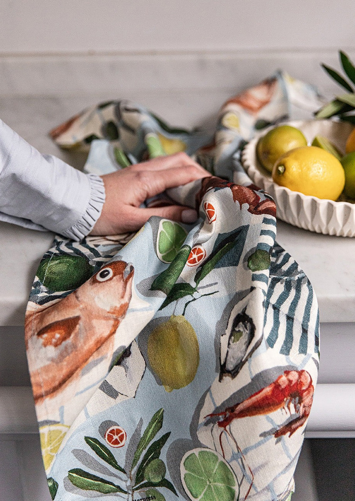 A printed linen tea towel with fish and citrus print.