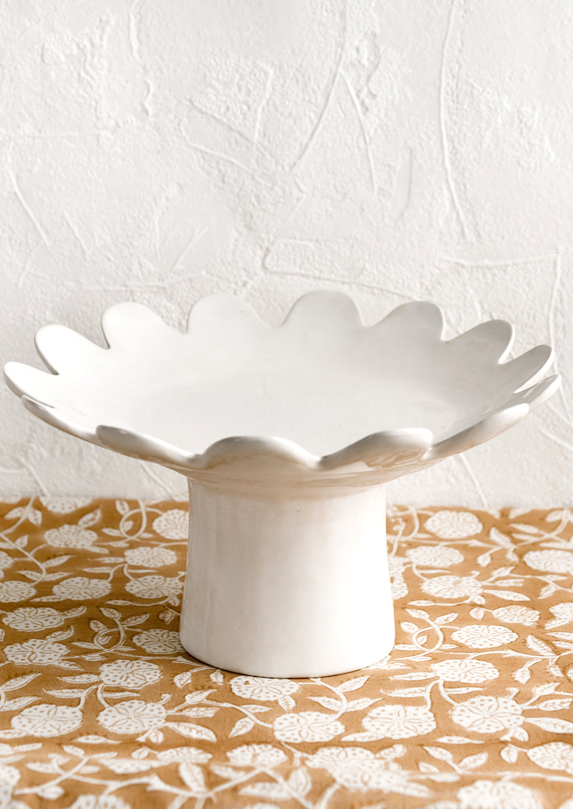 A pedestal riser in gloss white ceramic with scalloped plate shape.