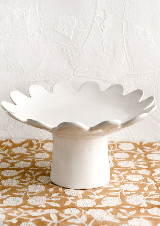 A pedestal riser in gloss white ceramic with scalloped plate shape.
