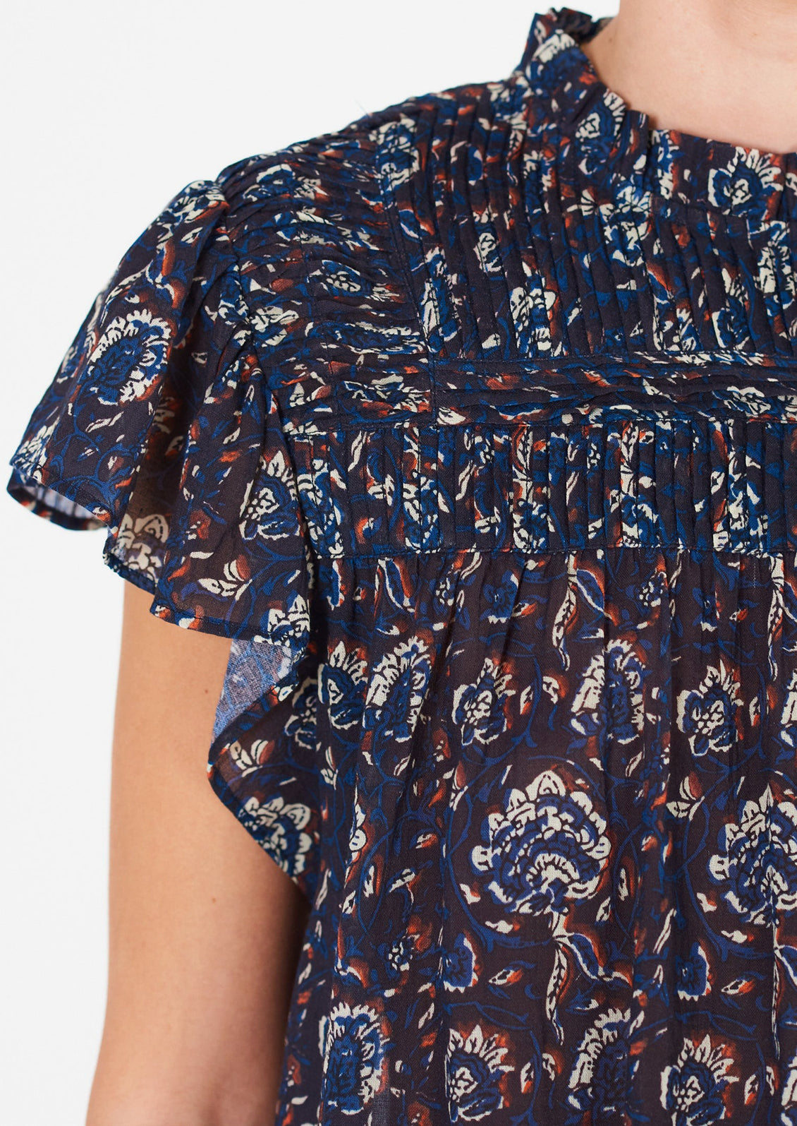 A woman wearing a blue, white and rust floral printed flutter sleeve top.