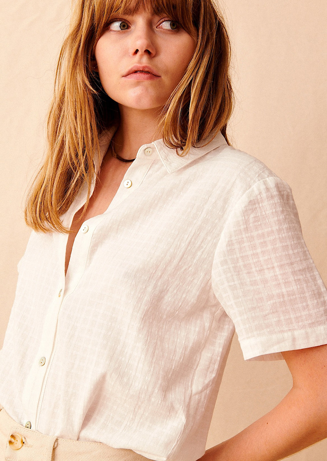 A woman wearing a short sleeve collared shirt with tonal grid texture.
