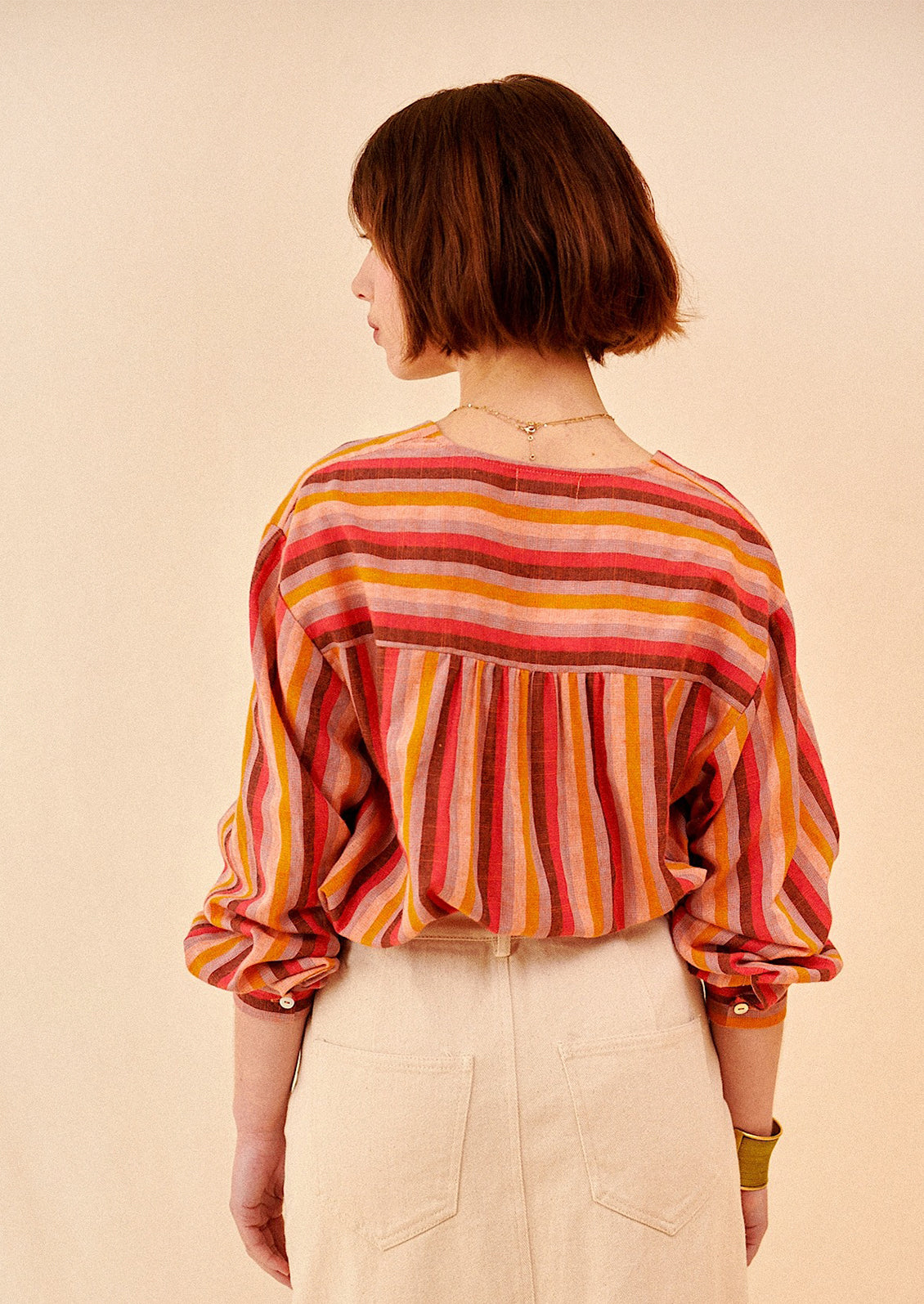 A woman wearing a v-neck, button front blouse in warm color stripe pattern.