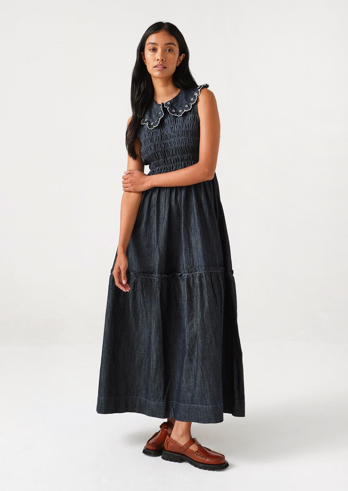 A woman standing wearing a long denim dress with an embroidered collar.