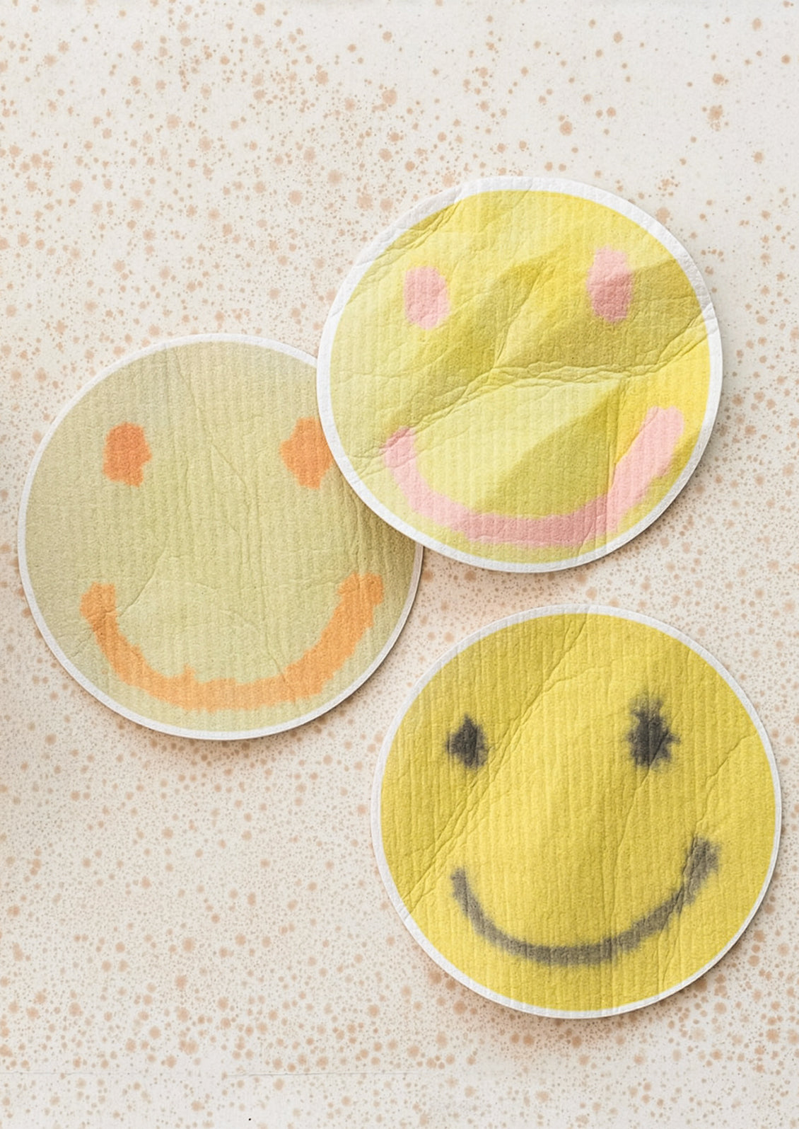 Three smiley face sponges on a textured surface