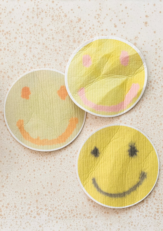 Three smiley face sponges on a textured surface