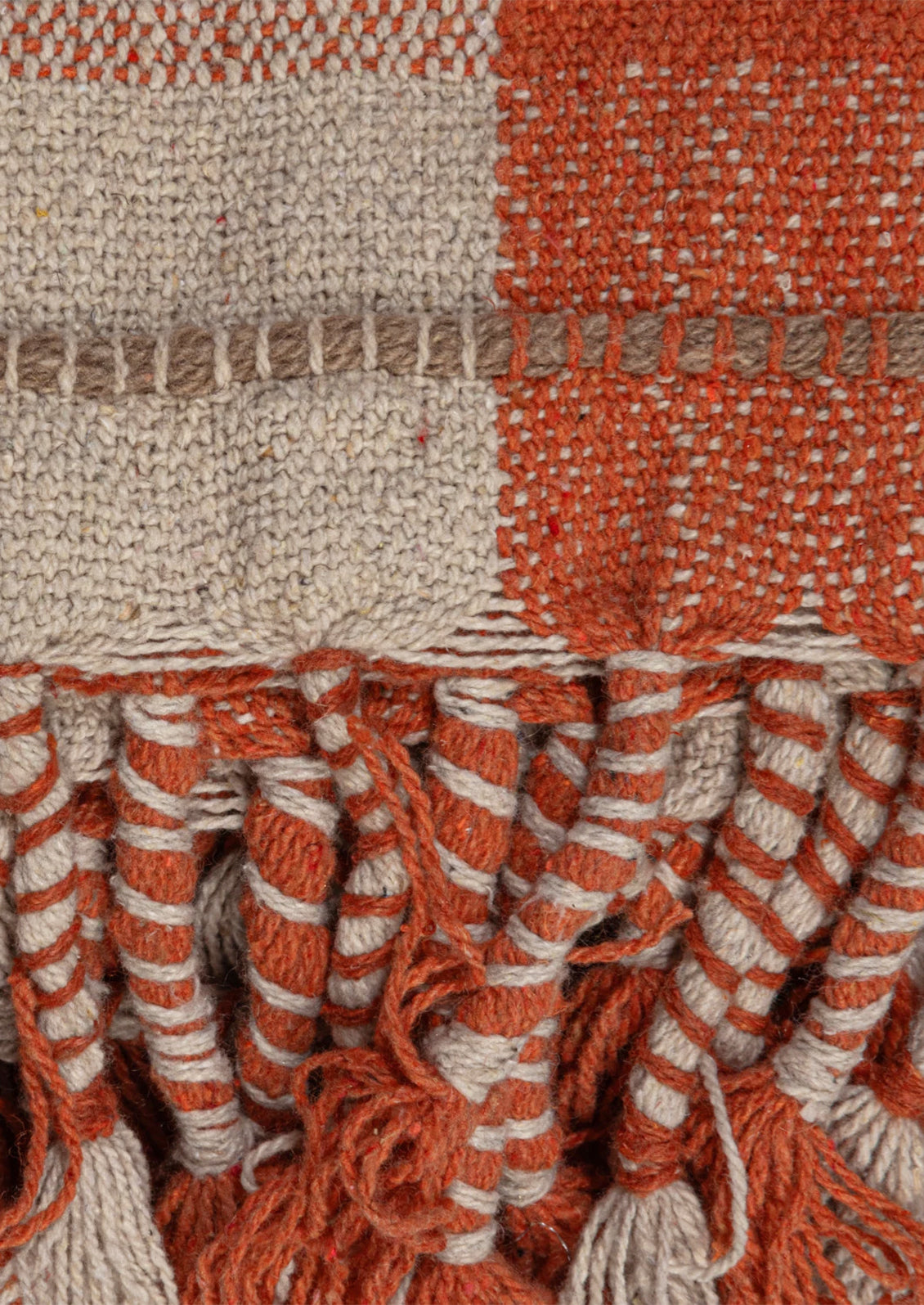 A cotton blend throw blanket in orange and cream plaid with multicolor tasseled stripe detailing.