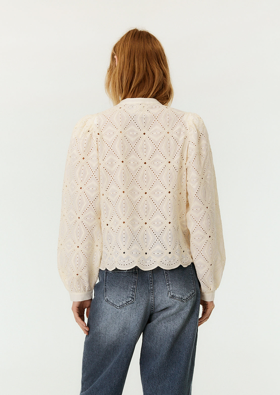 A woman wearing a cream lace blouse with long sleeves.