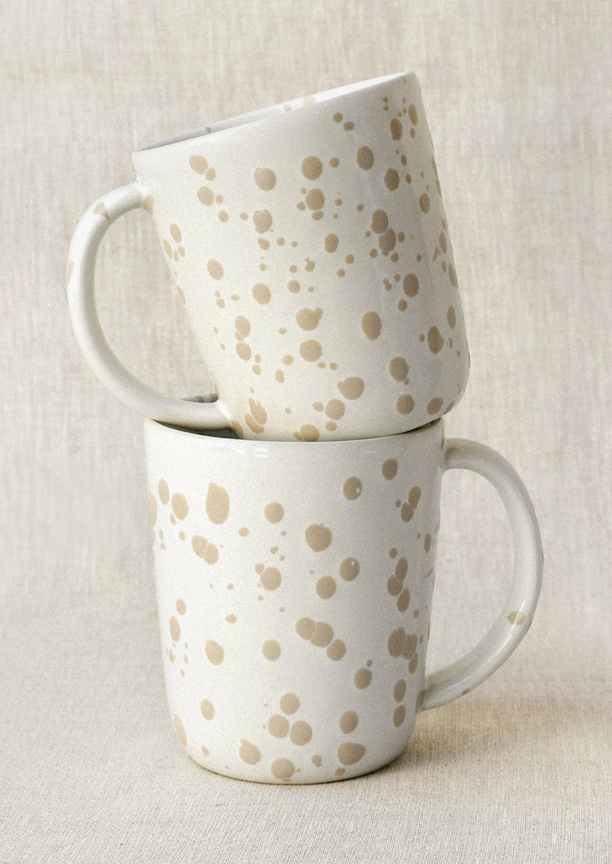Two white mugs with a brown paint splatter design stacked on top of each other.