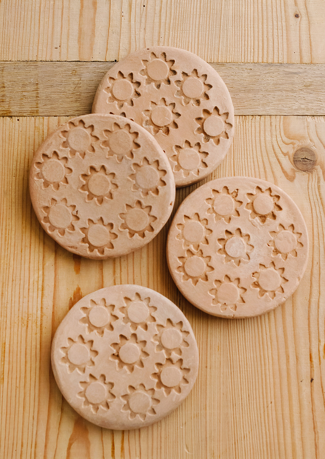 A set of round terracotta coasters with stamped sun pattern.