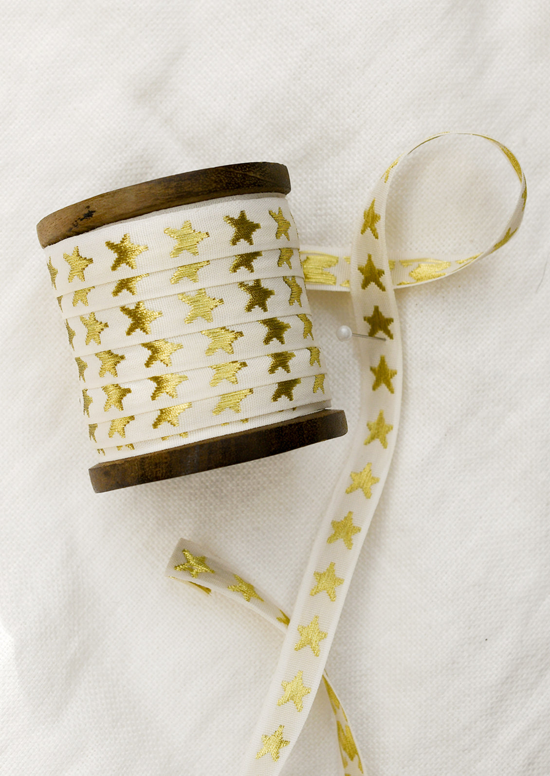 A walnut wood spool with cream ribbon with gold embroidered star pattern.