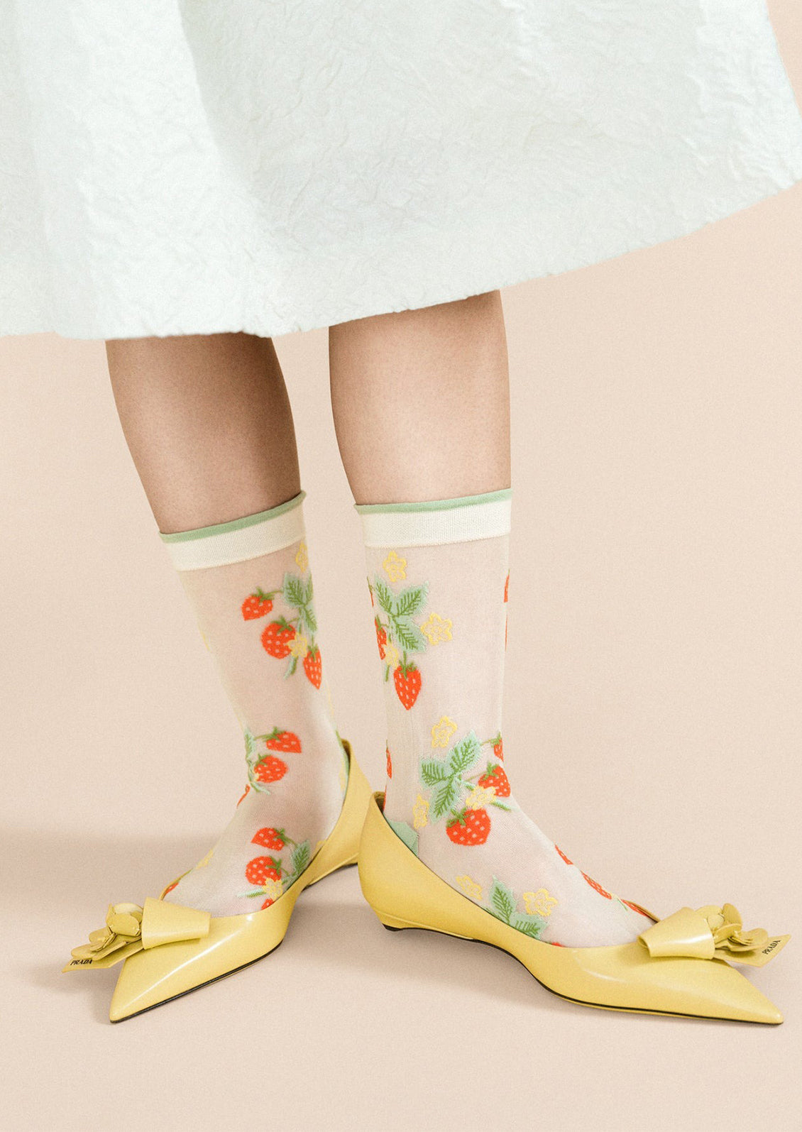 A woman wearing a sheer pair of socks with red strawberries, yellow flowers and light green trim.